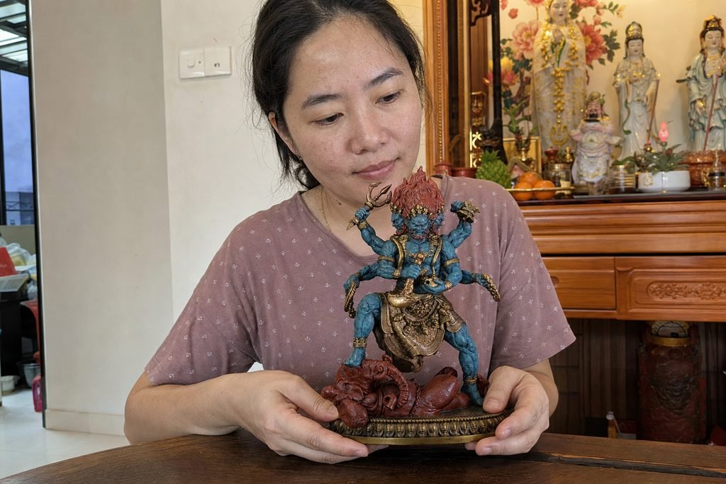 Six-armed Mahakala statue supported by a Malaysian Chinese woman in a home altar setting